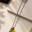 A silver-toned chain necklace with two geometric dog tag pendants, one textured silver and one brushed gold, displayed on a beige stone