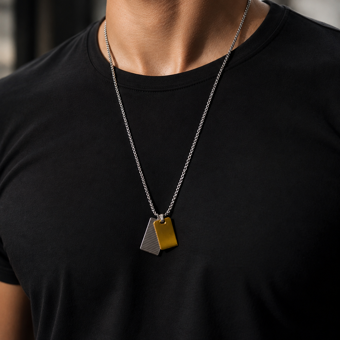man wearing a silver chain necklace with two overlapping geometric pendant tags, one yellow and one silver