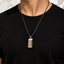 A man wearing a silver-toned chain necklace with a rectangular pendant featuring a white center and two gold triangular side accents